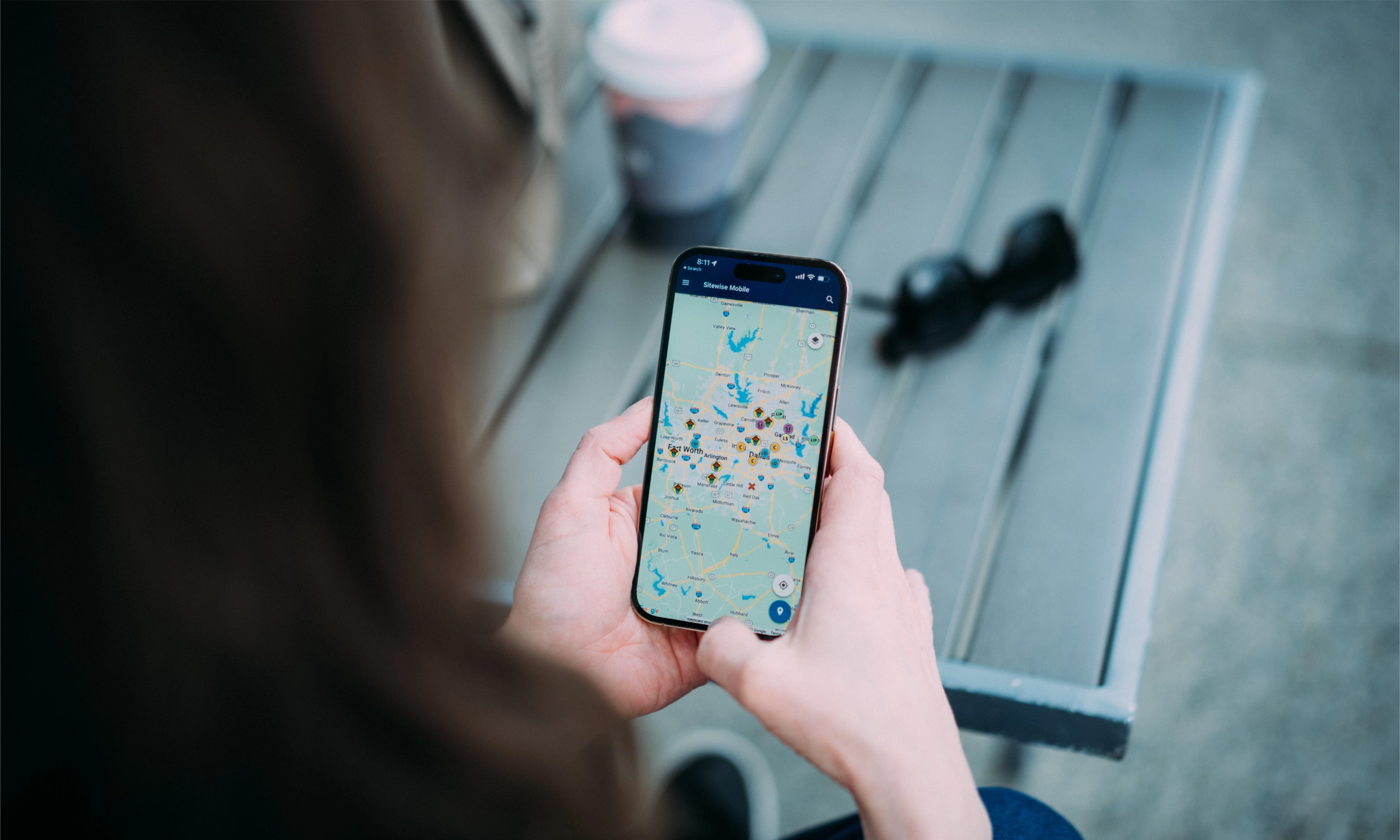 Person using Sitewise Mobile app outdoors on mobile phone while enjoying a quick coffee on site tours.